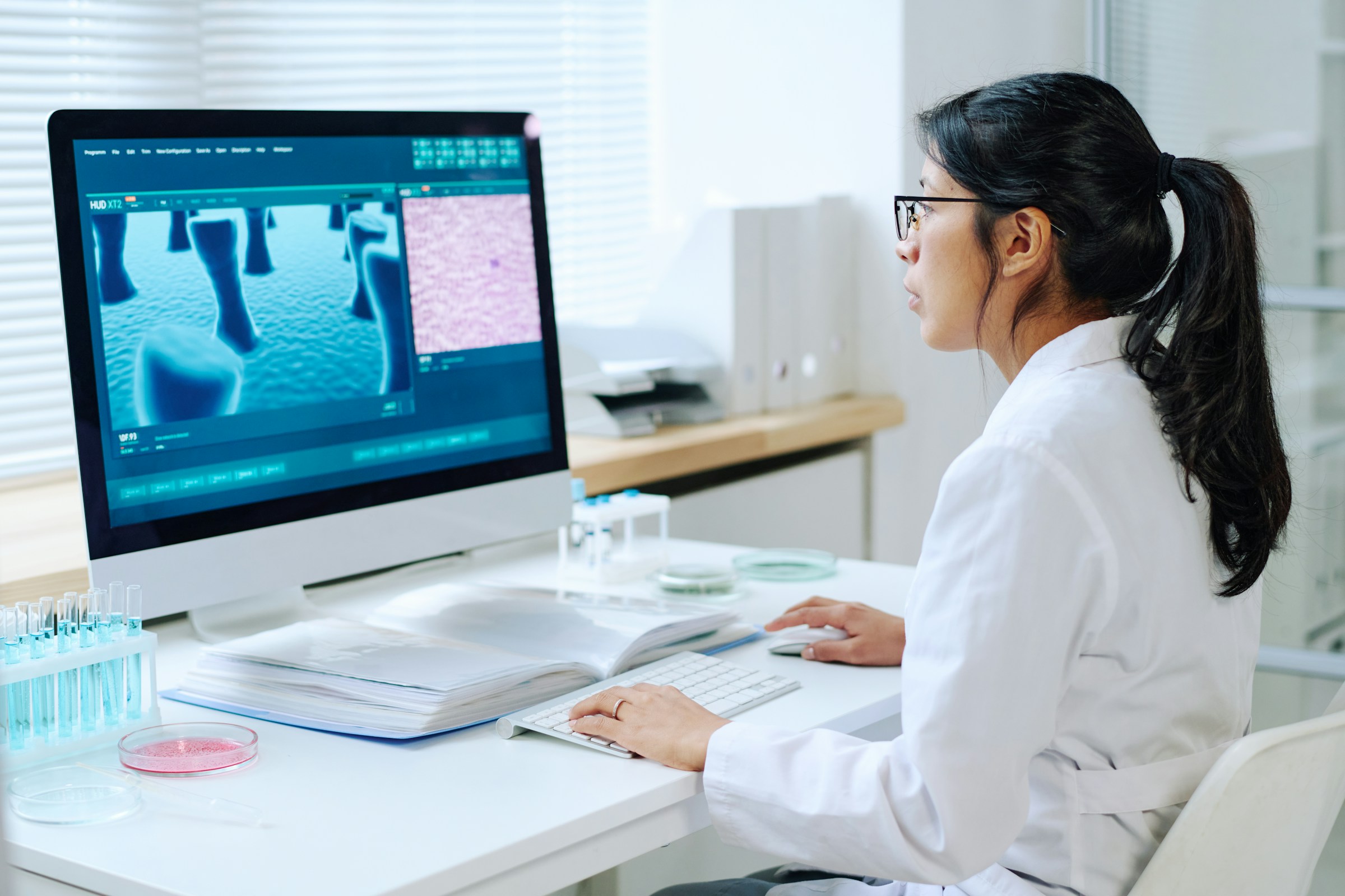 Scientist in a white lab coat analyzing microscopic images on a computer screen in a laboratory.